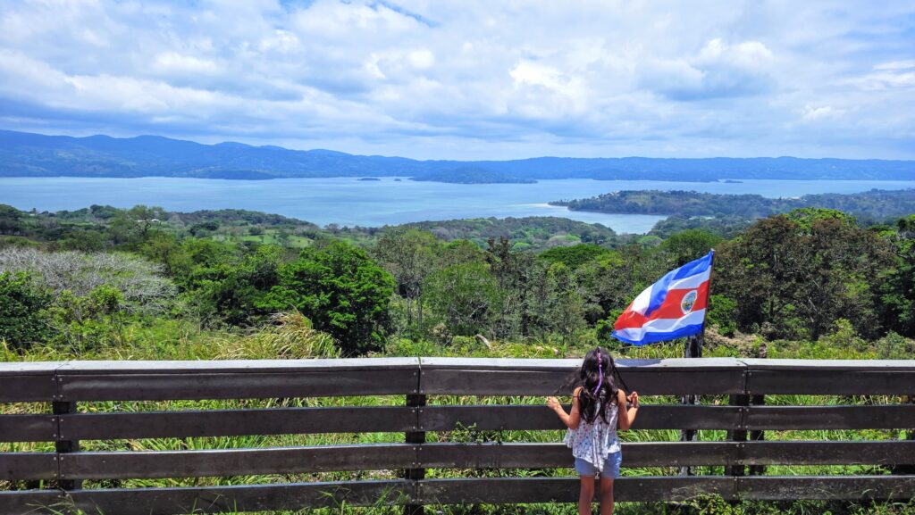 Costa Rica History and Culture for kids - girl looking at Arenal Lake with Costa Rica flag